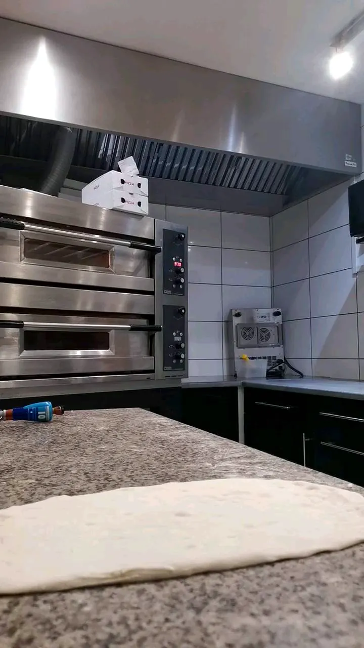 Cuisine de la pizzeria Mangio : fours à pizza en inox et plan de travail en granit avec une pâte étalée