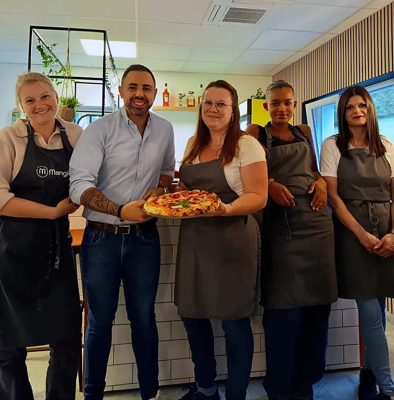 L'équipe de Mangio Pizza en tabliers dans la salle du restaurant, Massimo Bruno au centre tenant une pizza