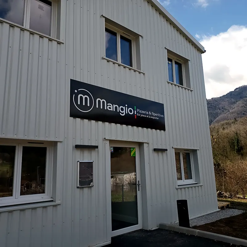 Façade du restaurant Mangio Pizzeria & Aperitivo à Saint-Jeoire, bâtiment blanc avec l'enseigne noire, au pied des montagnes de Haute-Savoie