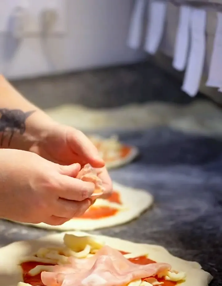 Le pizzaiolo garnit à la main des pizzas sur le plan de travail : sauce tomate, mozzarella et jambon