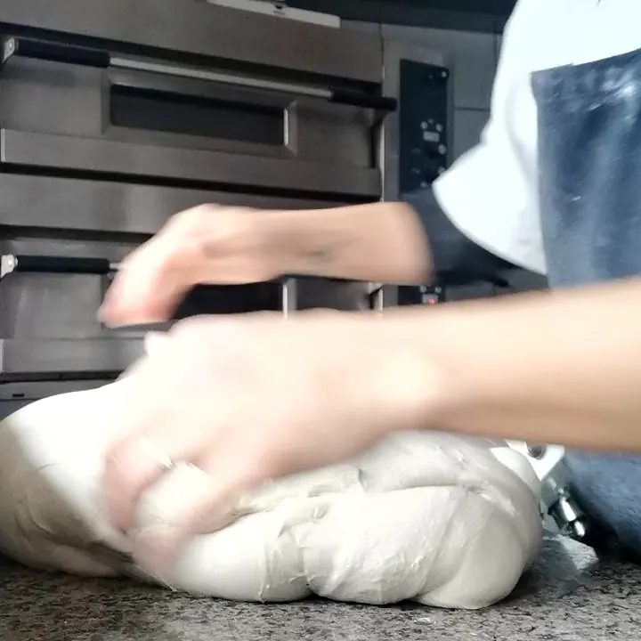 Pétrissage à la main de la pâte à pizza devant les fours de la pizzeria