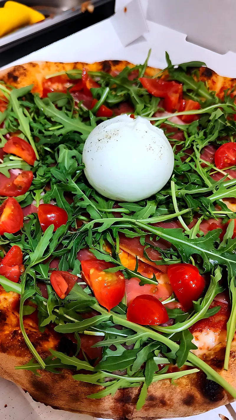 Pizza généreuse à la roquette, tomates cerises, jambon cru et burrata entière au centre