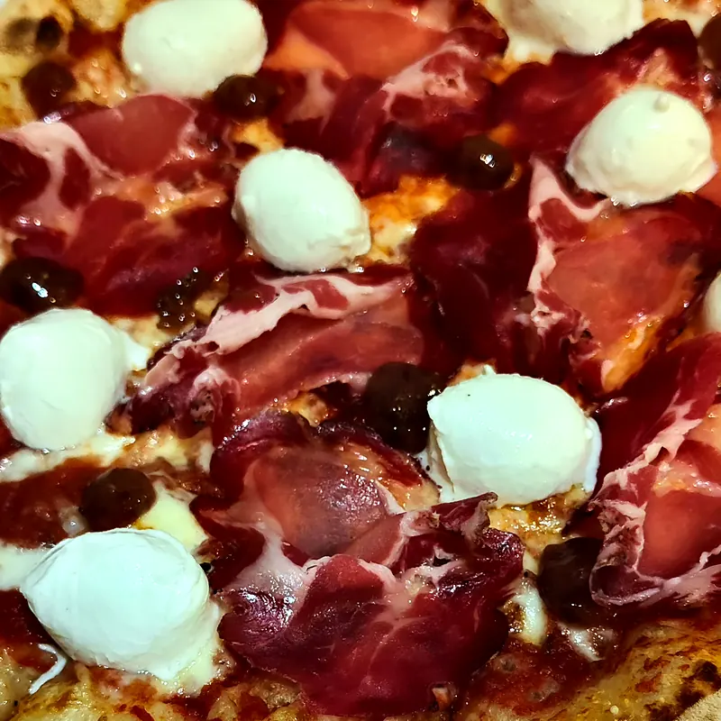 Gros plan d'une pizza au jambon cru, billes de mozzarella di bufala et olives