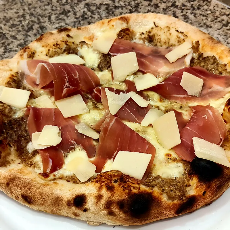 Pizza blanche crémeuse garnie de jambon cru et de copeaux de parmesan, pâte bien alvéolée cuite au four