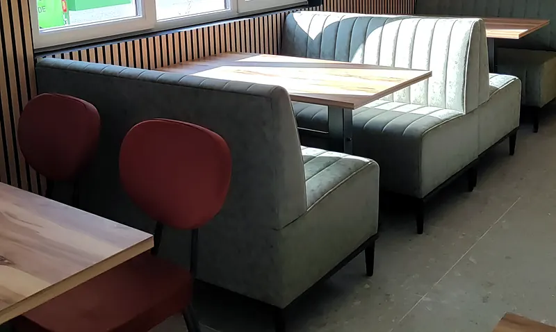 Salle du restaurant Mangio avec banquettes capitonnées grises, tables en bois clair et chaises bordeaux