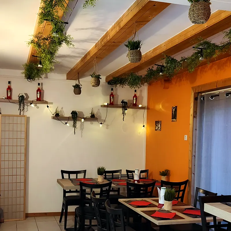 Salle chaleureuse au mur orange, poutres apparentes décorées de plantes suspendues et tables dressées en rouge